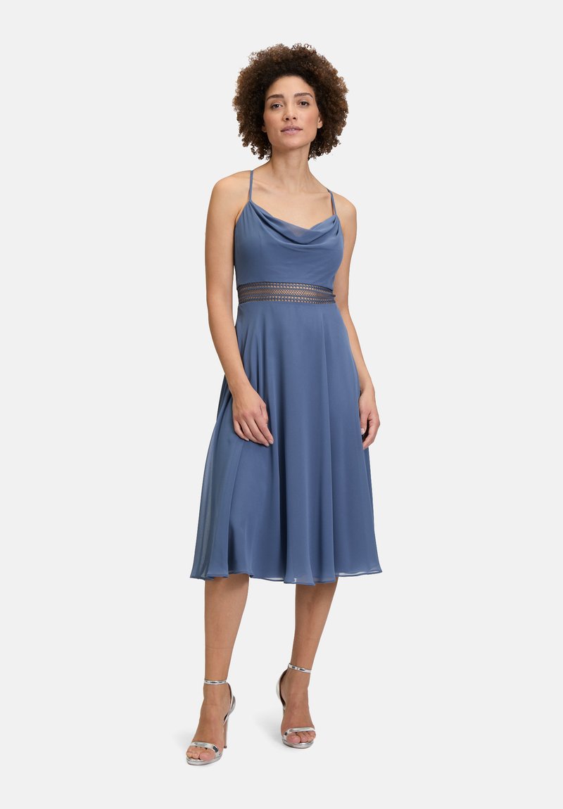 Robe sans manches à col montant en tissu bleu doux. Elle présente une taille cintrée avec une bande texturée. La jupe évasée atteint le milieu du mollet, élégante et fluide.