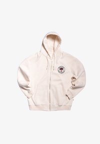 Sudadera con cremallera de color crema hecha de una tela suave. Presenta un bolsillo frontal y un logo circular con un diseño de árbol en la parte izquierda del pecho.