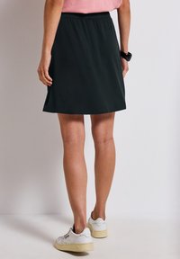Jupe noire, longueur genoux, avec une taille élastique, texture lisse et forme légèrement évasée. Portée avec des baskets blanches.