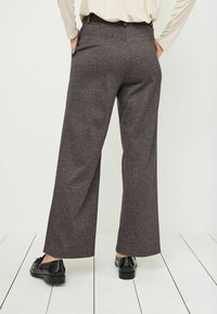 Grijze, gemêleerde wijde broek van wol met een gestructureerde afwerking, voorzien van zijzakken en een aansluitende tailleband, gecombineerd met zwarte kleding schoenen.