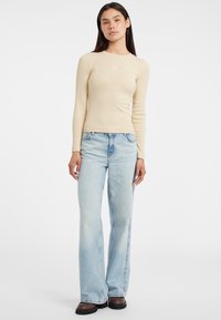 Maglietta beige a maniche lunghe abbinata a jeans a zampa d'elefante blu chiaro. La maglietta ha una texture liscia, mentre i jeans presentano un design classico a taglio dritto.