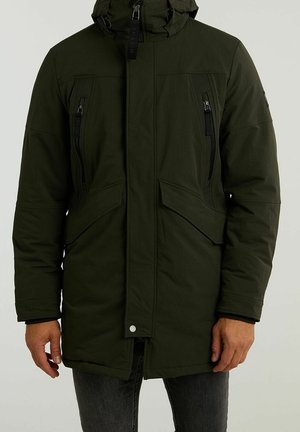 Parka verte foncée avec une fermeture éclair à l'avant, plusieurs poches zippées, une capuche et une coupe légèrement plus longue. Fabriquée en tissu isolant.