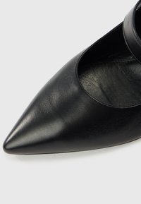 Μαύρο δερμάτινο παπούτσι με μυτερή μύτη και σχέδιο με κοψίματα. Ομαλή υφή, κομψή σιλουέτα και μινιμαλιστικό στυλ.