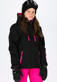 Giacca da sci nera con zip rosa, abbinata a guanti neri. La giacca è dotata di cappuccio e viene indossata con pantaloni rosa brillanti.
