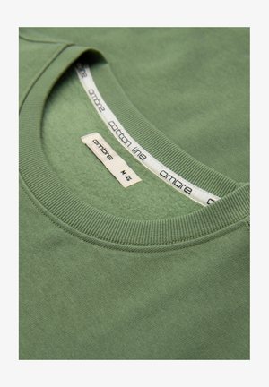 Grüner Baumwoll-Sweatshirt-Ausschnitt mit sichtbaren Markenetiketten mit der Aufschrift "ambre" und "cotton line", zeigt gerippten Kragenstich und weiche Stoffstruktur.