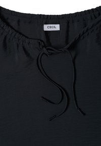 Ceinture élastique noire avec cordon de serrage sur un vêtement en tissu, avec une étiquette blanche comportant le texte "CECIL".