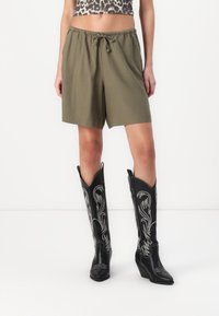Olivengrønne shorts med elastisk talje og snørebånd. Sorte cowboyboots med sølvbroderi og spiss tupp.