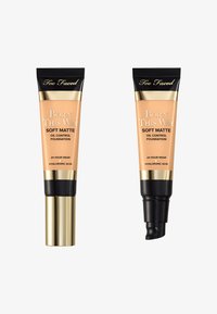 Two tubes of "Born This Way Soft Matte Oil Control Foundation" by Too Faced. One has a gold cap, the other a black pump, both with beige product.