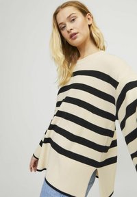 Bež in črn striped ohlapen pulover z rebrasto teksturo, širokimi rokavi, stranskimi razpoki in okroglo ovratnikom. Nošen z modrimi kavbojkami.