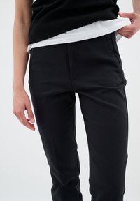 Black tailored pants with a sleek design, featuring a smooth texture and subtle front crease. Worn with a black and white layered top.