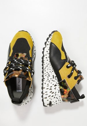 Masywne sneakersy z żółtą zamszową skórą, czarną siateczką, wzorem w panterkę oraz białą podeszwą z czarnymi plamkami i czarno-białymi sznurowadłami.
