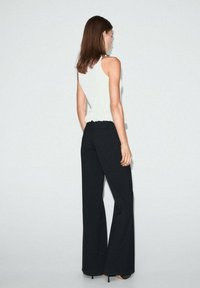 Top alb fără mâneci cu volan la margine, purtat cu pantaloni negri cu croială largă. Textură netedă și design ajustat. Tocurile adaugă înălțime.