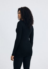 Zwarte longsleeve top van gladde stof, aansluitende pasvorm en ronde halslijn. Gecombineerd met bijpassende zwarte leggings.