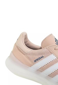Baskets Adidas Spezial beiges avec des bandes blanches en zigzag et une semelle translucide texturée.