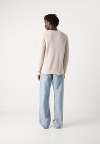Beige long-sleeve sweater with a textured finish, paired with light blue wide-leg jeans featuring visible stitching and back pockets.