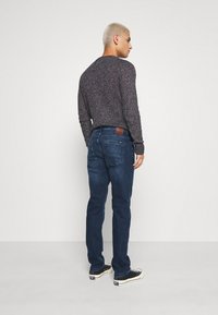 Donkerblauwe denim jeans met een rechte snit, voorzien van achterzakken en een bruin leren label op de tailleband. Ggedragen met een gebreide trui met textuur.