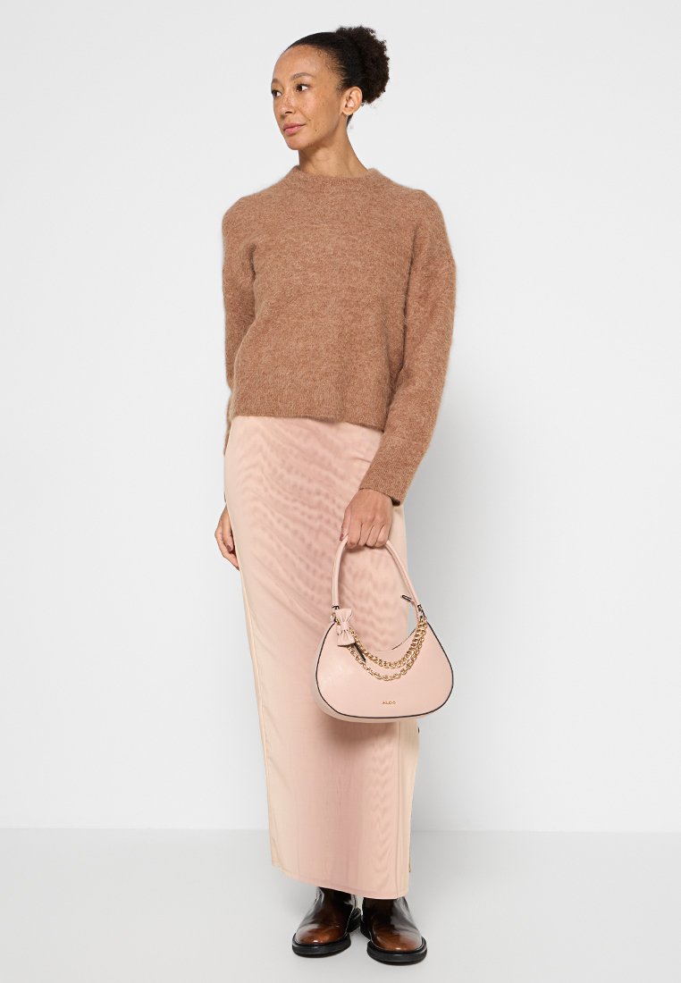 Un pull en laine marron, une jupe maxi rose pâle et un sac à main rose clair avec des détails en chaîne dorée. Des bottines noires à talons complètent l'ensemble.