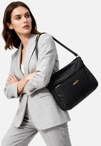 Borsa a tracolla nera trapuntata di forma rettangolare. Presenta dettagli in oro e un logo del marchio prominente, disegnato con un motivo ripetuto.