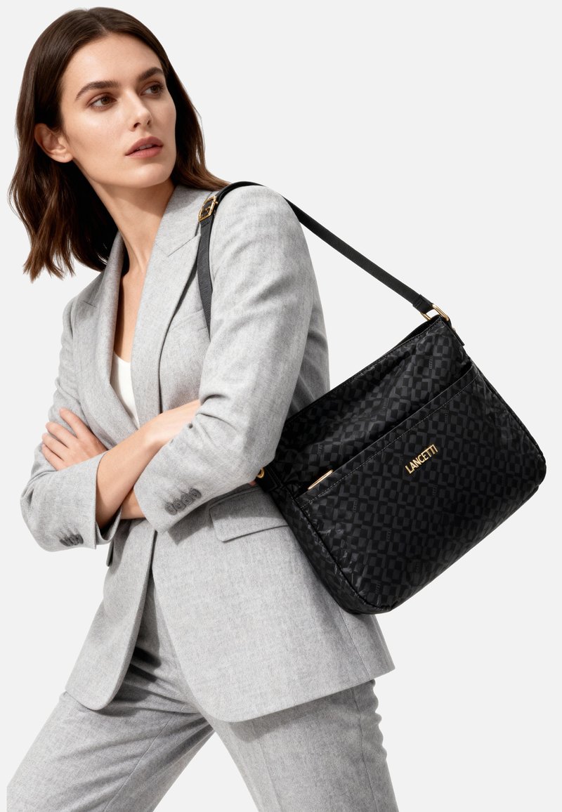 Borsa a tracolla nera trapuntata di forma rettangolare. Presenta dettagli in oro e un logo del marchio prominente, disegnato con un motivo ripetuto.