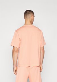 Short-sleeve, crew-neck t-shirt in light peach color, made of textured fabric with a relaxed fit and slightly dropped shoulders.