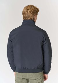 Giubbotto bomber blu navy con collo alto, struttura imbottita, polsini e orlo a coste. Tessuto liscio, design semplice, adatto per un abbigliamento casual.