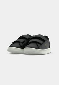 Scarpe nere in materiale sintetico con due cinturini in Velcro, suola in gomma bianca, forma arrotondata e un accento del logo verde sul lato.