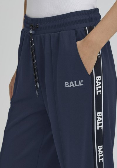 Pantalons de sport bleu marine avec une taille élastique, des poches latérales et un cordon de serrage à motif. Présente des accents de logo et de stripes blancs.