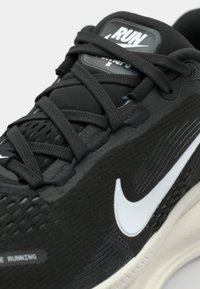 Schwarzer Sportschuh mit strukturiertem Obermaterial, weißem Swoosh-Logo und schwarzen Schnürsenkeln. Verfügt über eine gepolsterte Sohlen und Mesh-Details für Atmungsaktivität.