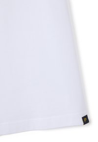 Weißer Stoff mit genähtem Saum und einem kleinen schwarzen Etikett am unteren Rand, das mit einem gelben Buchstaben "P" beschriftet ist.