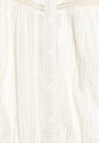 White blouse with thin vertical stripes, textured fabric, lace detailing near the shoulders, and five buttons down the front.