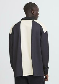 Langærmet polo skjorte med et sort og creme farveblok design, lavet af blødt stof med en afslappet pasform og en klassisk krave.