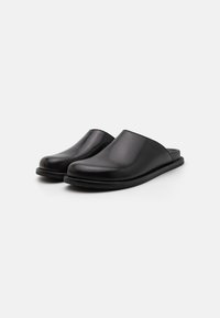 Sorte lær slip-on klipklapper med en glat overflade, rund tå, lav profil og fleksibel gummisål. Minimalistisk design, ingen synlig hardware.