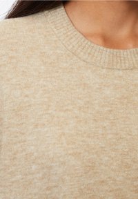 Pull en maille beige avec un col rond côtelé, une texture douce et un motif chiné subtil, mettant l'accent sur la chaleur et le confort.