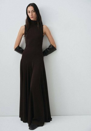 Abito lungo, aderente, marrone con collo alto e orlo svasato. La modella indossa guanti neri lunghi, con tessuto liscio e design minimalista.