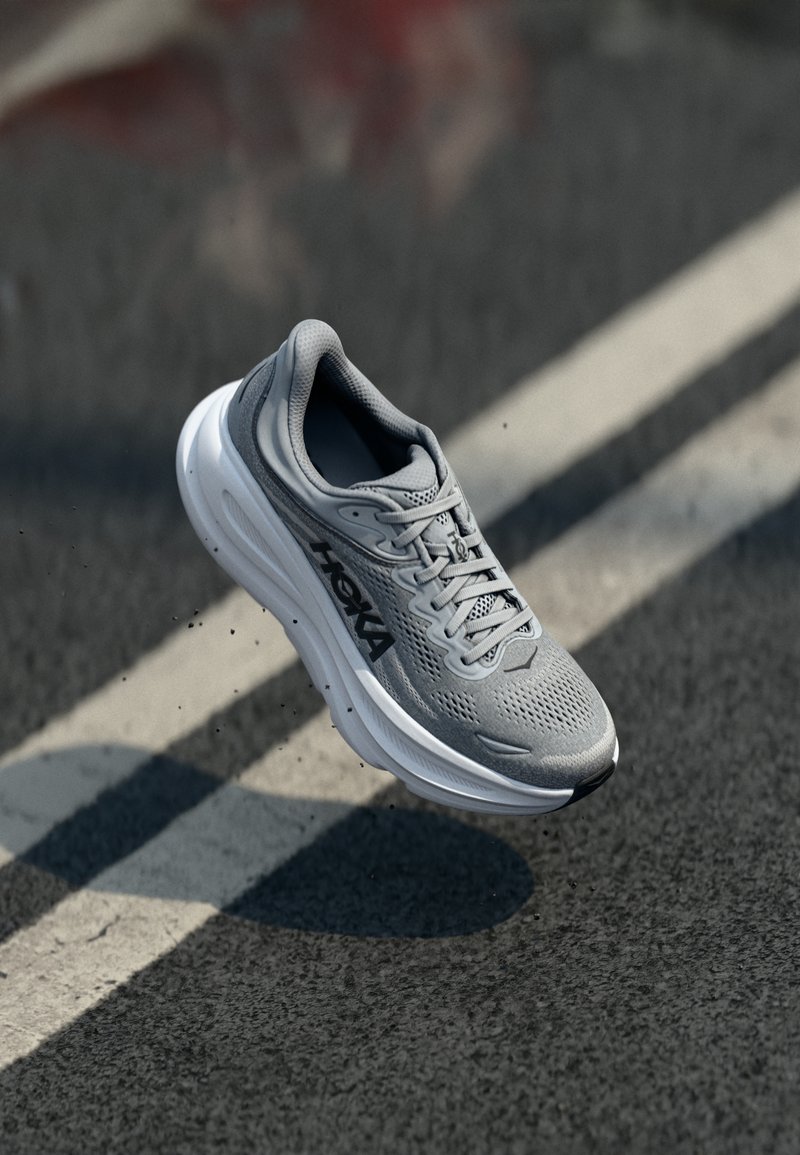 Graue Sportschuhe mit Mesh-Obermaterial, gepolstertem Schaft und weißer Sohle. Verfügt über ein schwarzes Logo und eine strukturierte Verzierung an der Oberseite.