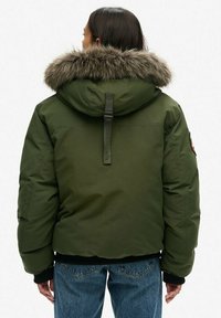 Green puffer jacket with a fur-lined hood, featuring a thick texture, adjustable straps, and ribbed cuffs. Back view shows a relaxed fit.