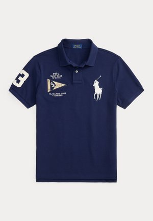 Polo bleu marine avec logo joueur de polo brodé en blanc, texte yacht club, écusson drapeau nautique et numéro 3 sur la manche droite.