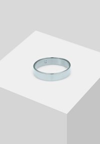 Sølvmetalring med en glat, poleret overflade og en rund kant. Præsenteret på en lys grå sokkel med et minimalistisk design.