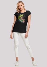 Schwarzes kurzärmliges T-Shirt mit einem bunten floralen Grafikdesign. Das Modell trägt weiße Skinny Jeans und weiße Sneakers und steht lässig.