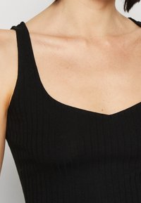 Černý žebrovaný top bez rukávů s hlubokým V-výstřihem a širokými ramínky. Hladká textura s jemnými švy.
