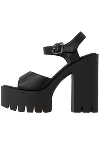 Sandalias de plataforma negras con tacón grueso, que cuentan con un upper texturizado, punta abierta, correa de tobillo ajustable y suela serrada.