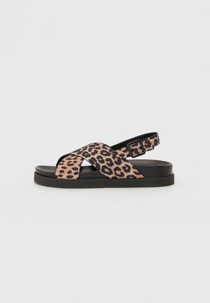 Leopard print sandal with cross straps, black accents, adjustable buckle, and flat sole. Soft material with a textured surface.