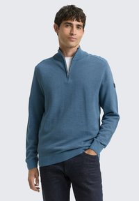 Blauer Reißverschluss-Pullover mit strukturiertem Oberfl�äche, gerippten Bündchen und Stehkragen, kombiniert mit dunklen Jeans.