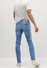 Vaqueros de mezclilla de color azul claro, diseño ajustado, con una etiqueta beige en la cintura trasera y dos bolsillos traseros. Combinados con zapatos blancos.