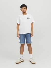 Vit bomull T-shirt med en logotyp på vänster bröst, ihopparad med ljusblå denimshorts. Skorna är i krämfärgad med bruna sulor.