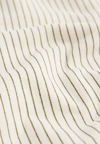 Pleteni tekstil s kremasto ozadjem in navpičnimi zelenimi črtami, ki ustvarjajo teksturiran, rebrast učinek.