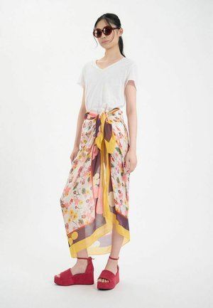 Jupe en tissu léger à motif floral avec une taille nouée dans des couleurs pastel et des accents jaunes, accompagnée de sandales à plateforme rouges.