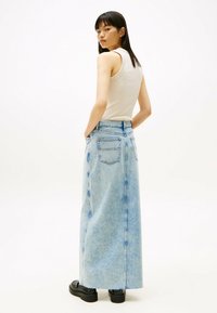 Lichtblauwe denim maxi rok met een rechte silhouet, achterzakken en een rafelige zoom, gecombineerd met een aansluitend crèmekleurig tanktop en zwarte schoenen.