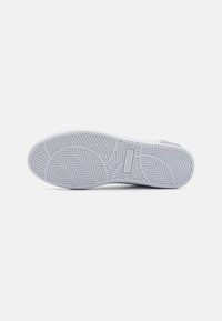 Suola di sneakers bianche con finitura in gomma testurizzata caratterizzata da motivi a spina di pesce e ondulati; dettaglio logo in rilievo vicino al tallone.