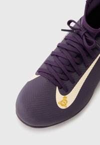 Fialová futbalová obuv s textúrovaným zvrškom, so smotanovým Nike swooshom a žltým logom '93' na boku. Šnúrky v zodpovedajúcom fialovom odtieni.